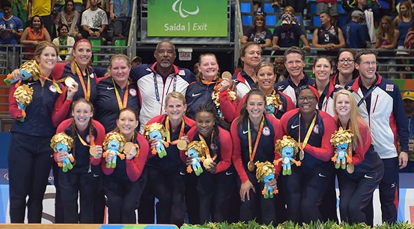 The U.S. women's sitting national team poses for a photo. The athletes have gold medals around their necks and are holding a Rio 2016 stuffed animal.