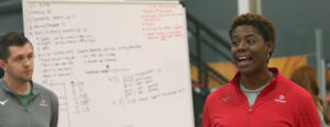 Female coach in front of a whiteboard talking to athletes