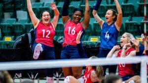Three female volleyball players iin red cheer with their arms in the air