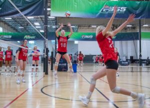 A female volleyball sets the ball while another goes up to hit
