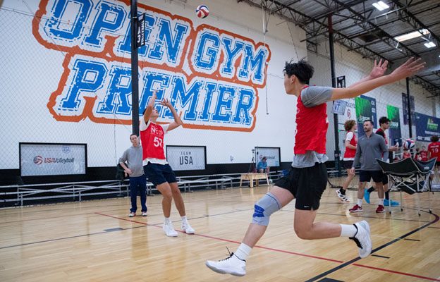 A male volleyball player sets the ball while one goes up to hit