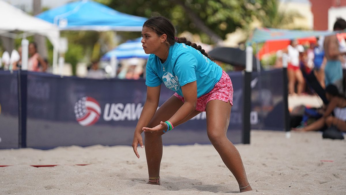 A girl readies to receive a serve on the sand