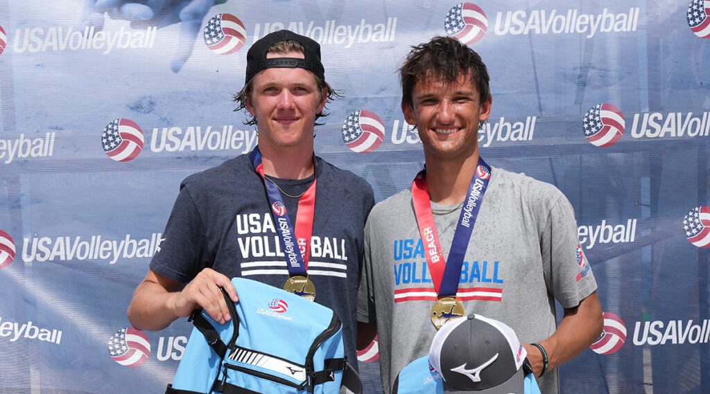 Two boys hold backpacks and wear medals as winners of 18 Open at beach nationals