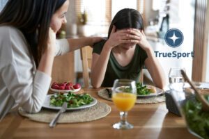 A mother and daughter at a dinner table with the mom comforting the girl