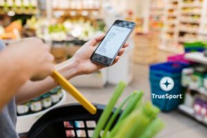 A shopping bag with food in it while a woman looks at hr iphone
