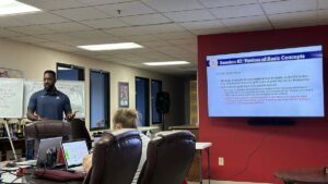 Brandon Robinson stands in front of other coaches with a powerpoint that says Basic Concepts