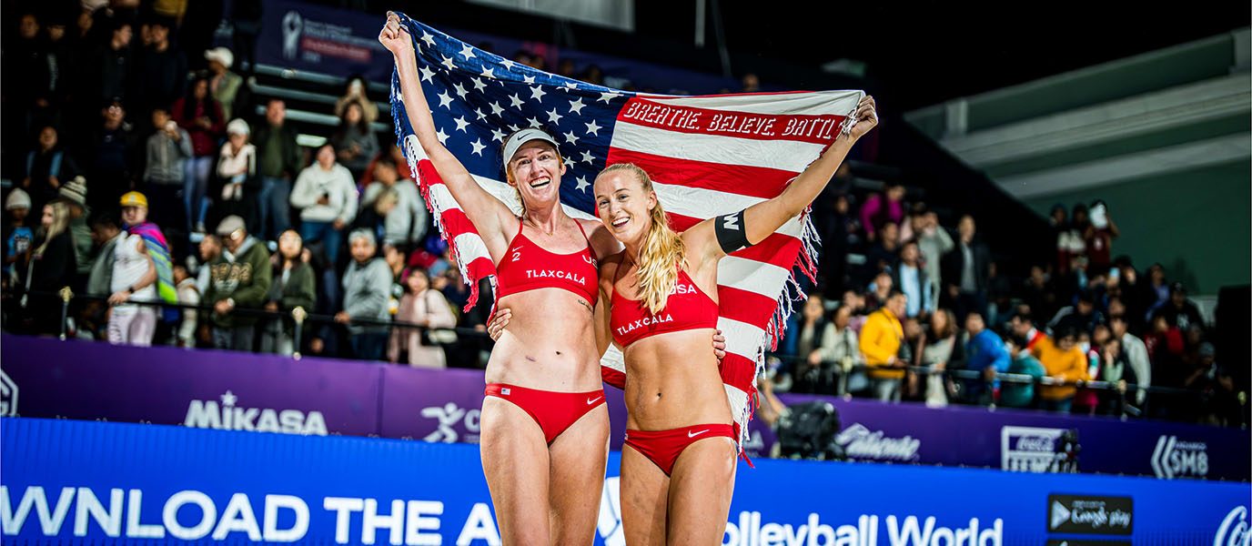 Kelly Cheng and Sara Hughes hold up the American flag on the sand