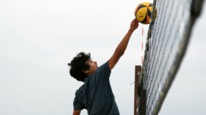 An athlete attacks a volleyball while it's above a volleyball net.
