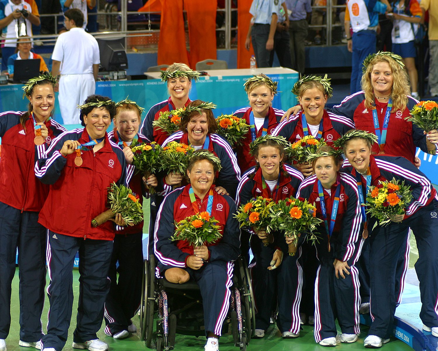 The 2004 U.S. Women's Paralympic Sitting Volleyball team members pose for a photo with their bronze medals and the American flag.