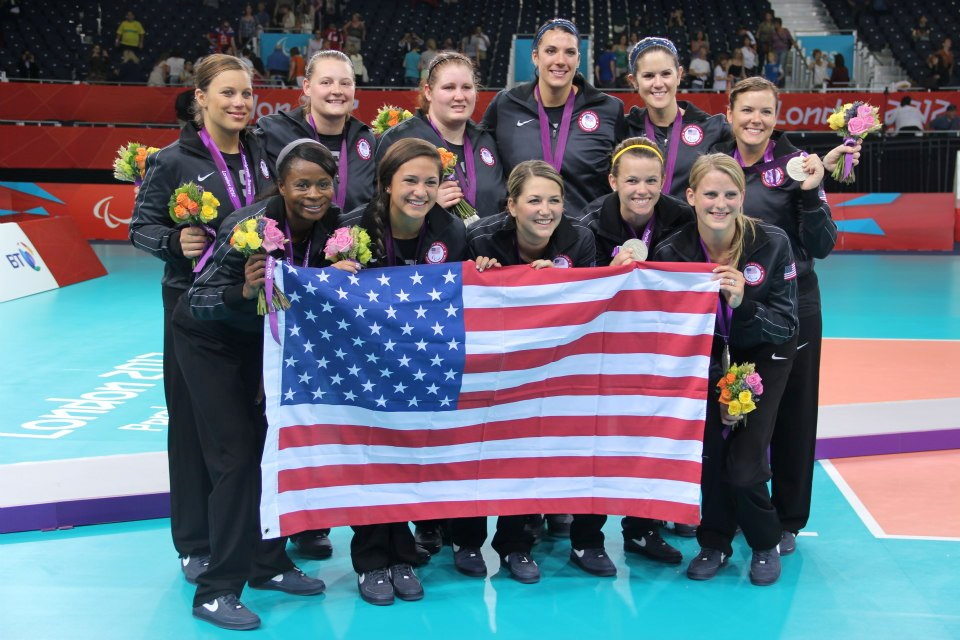 The 2012 U.S. Women's Paralympic Sitting Volleyball team members pose for a photo with their silver medals and the American flag.
