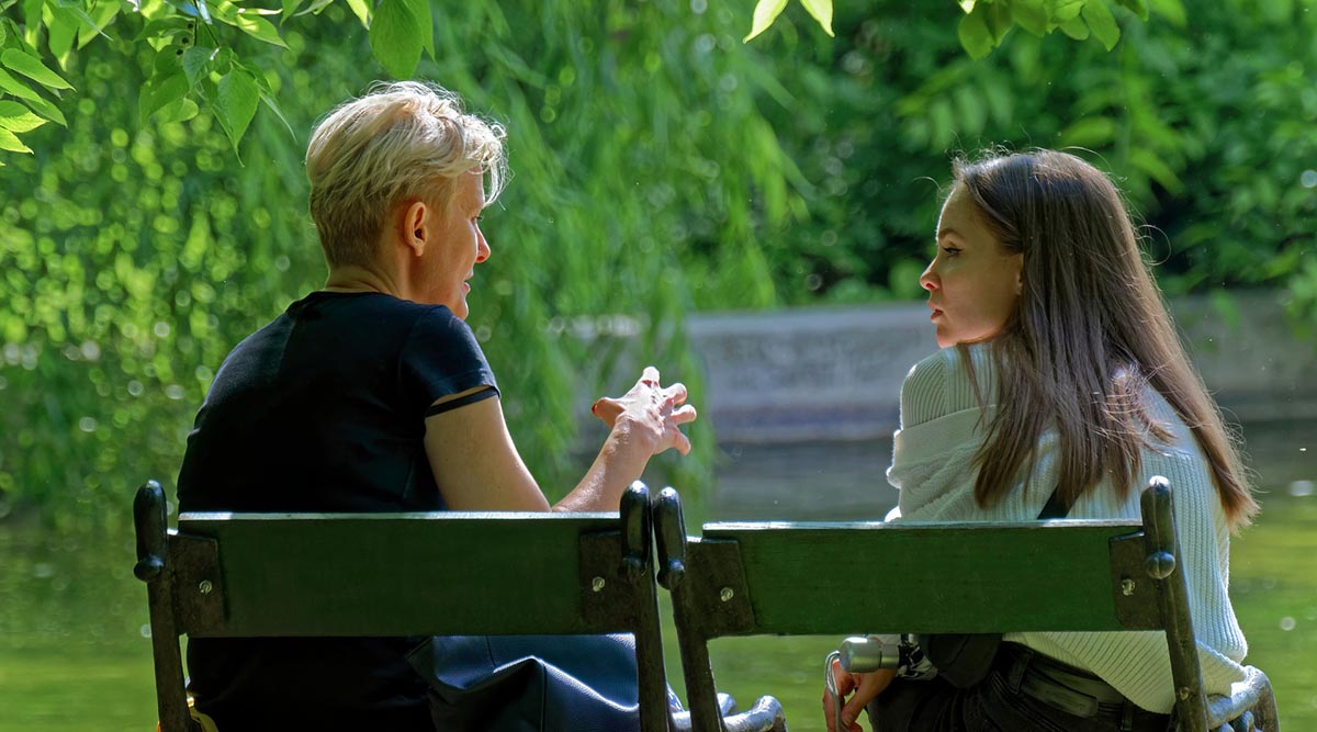 A woman and girl have a discussion on a park bench