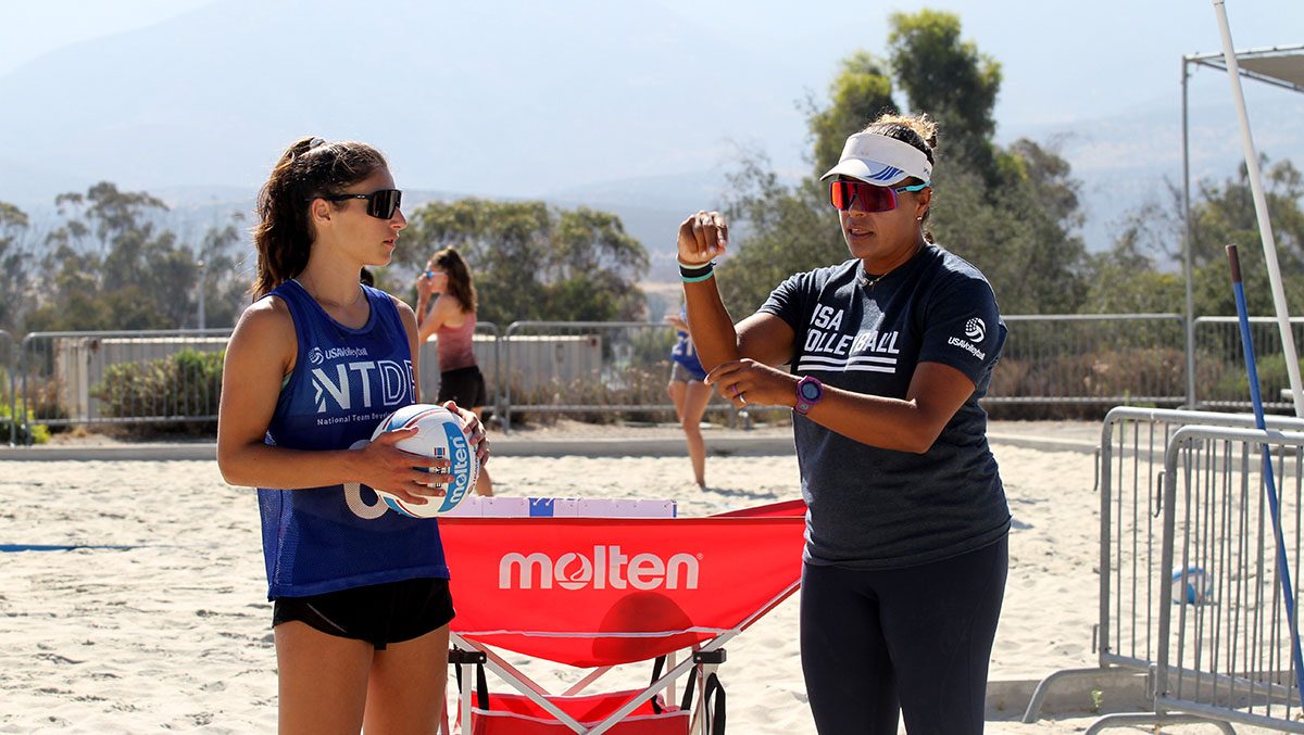 A coach instructs a female athlete on the beach