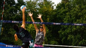 A men's beach volleyball player goes up for an attack with a player on the other side of thee net up for the block