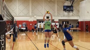 A female athlete sets the ball while another is ready to go up for a hit