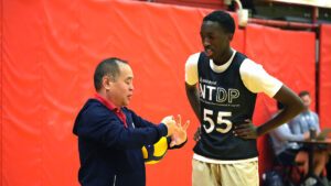 A male coach talks to a young male athlete about setting at the NTDP training series