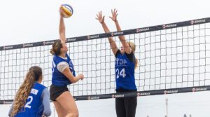 A girls beach player is up for a block against a girl attacking