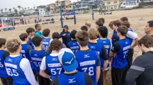 A group of boys beach athletes gather around a coach