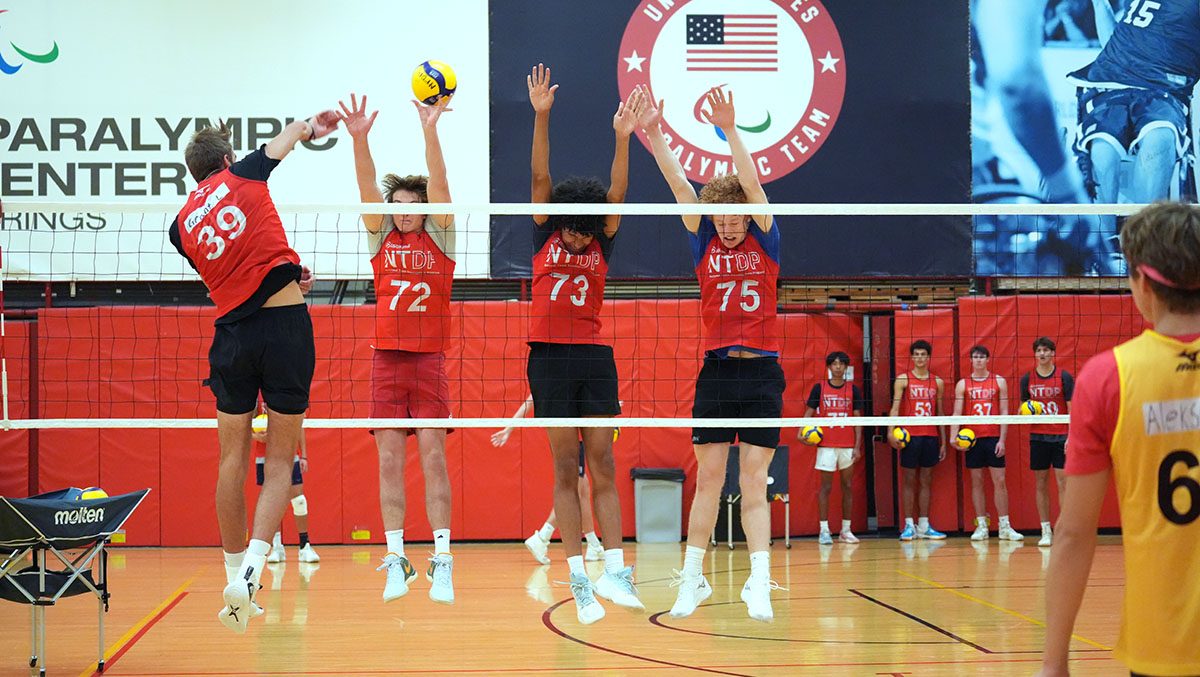 A male boys indoor player attacks the ball with a triple block