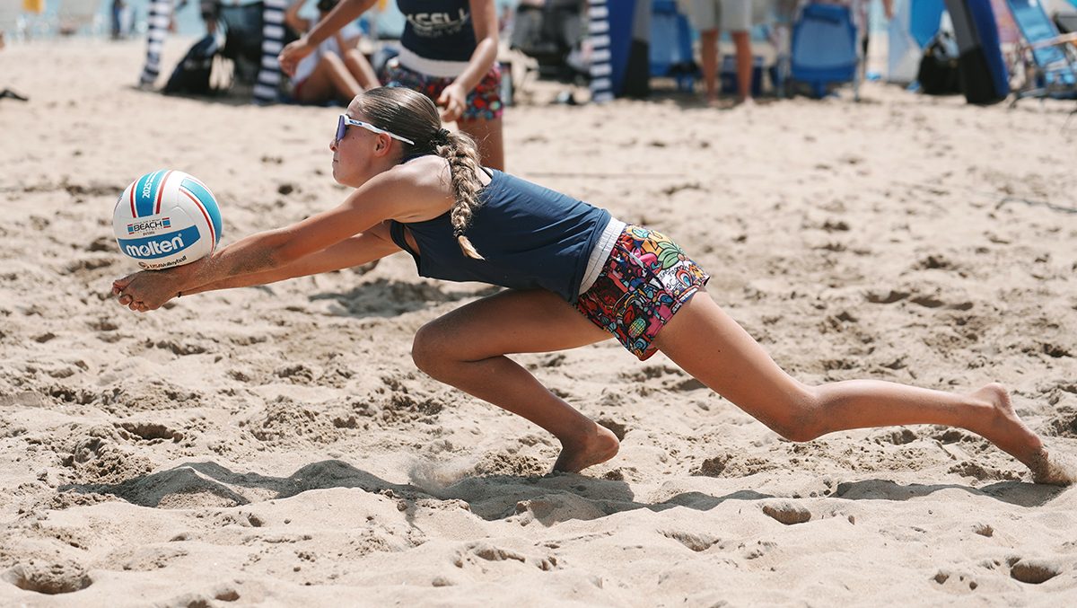 A girls beach volleyball player dives for a dig